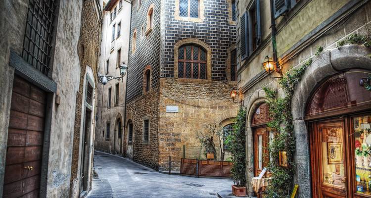 Smalle steenstraatje in Florence omzoomd door stenen en bakstenen Renaissance-gebouwen met gewelfde deuren en warme straatlantaarns.
