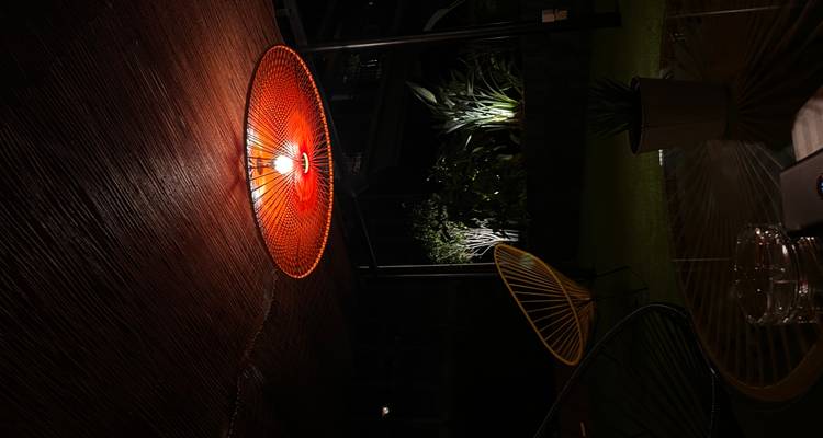 Salon faiblement éclairé présentant un luminaire de plafond rouge tissé frappant et du mobilier extérieur moderne la nuit.