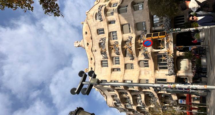 Vue au niveau de la rue de la façade en pierre distinctive de la Casa Milà avec des touristes et la circulation urbaine sous un ciel bleu.