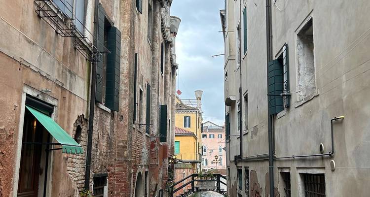 Une ruelle vénitienne étroite entre de hauts bâtiments s'ouvrant vers un petit pont en arc.
