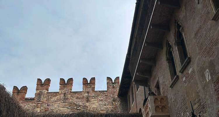 Mur de briques crénelé et fenêtres supérieures de la cour de la maison de Juliette sur fond de ciel pâle.