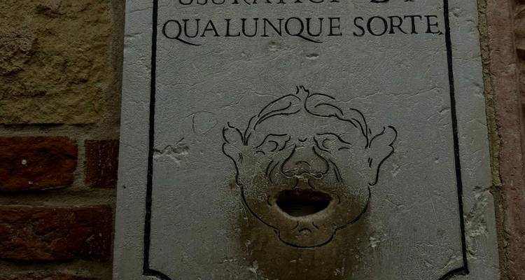 Plaque de pierre avec un visage gravé et une inscription italienne sur un mur extérieur.