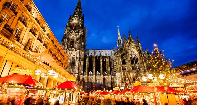 Festive Cologne Christmas market glowing beneath towering Cologne Cathedral at dusk