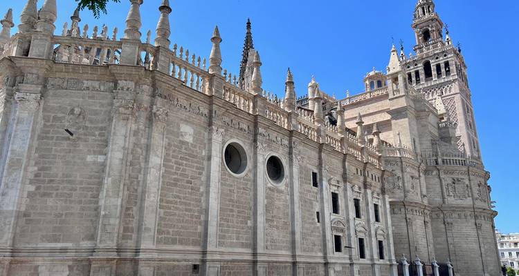 Vue latérale de la Cathédrale de Séville et de la tour Giralda qui s'élève majestueusement contre un ciel bleu éclatant.