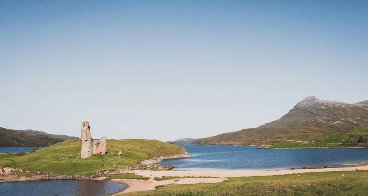 Las ruinas del Castillo de Ardvreck se alzan en una loma cubierta de hierba que sobresale en un loch azul.