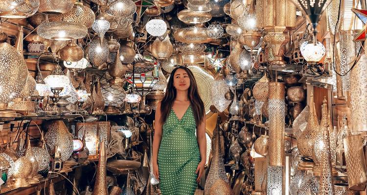 Vrouw in groene jurk omringd door een schitterend assortiment koperen lampen en lantaarns in een Marokkaanse souk.