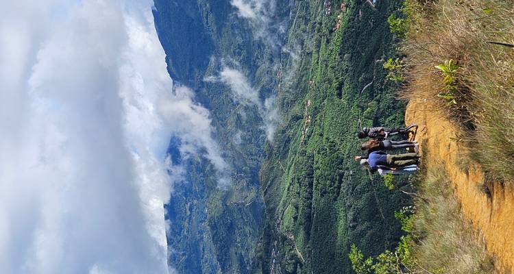 Un pequeño grupo de pie en una cresta con vistas a un amplio valle verde con nubes flotando abajo.