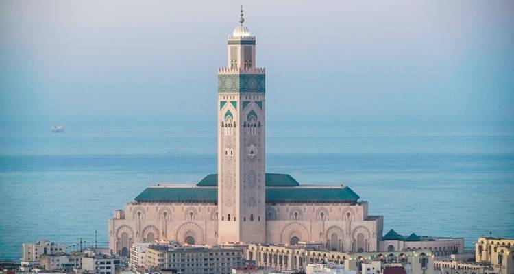 Vista lejana de la Mezquita Hassan II elevándose desde la costa del Atlántico contra un cielo azul y brumoso.