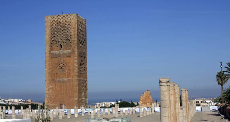 La Torre Hassan de ladrillo rojo se eleva imponente junto a filas de columnas de piedra sin terminar bajo un cielo azul despejado.