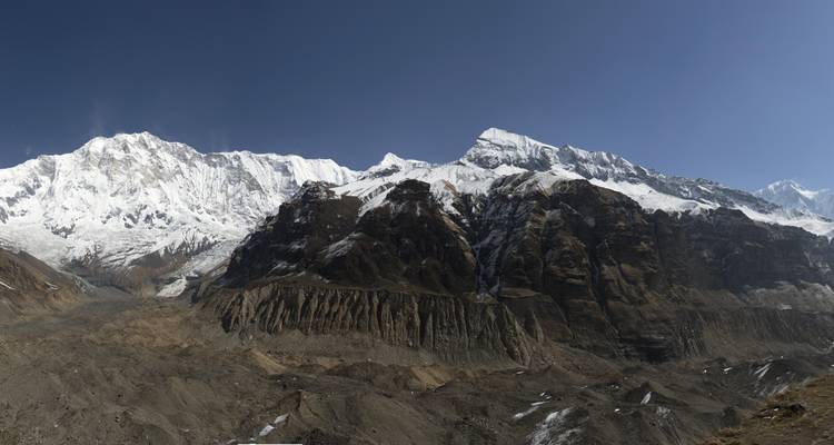 Breed panoramisch uitzicht op de ruige, sneeuwbedekte toppen en rotswanden van het Annapurna-gebergte onder een heldere hemel.