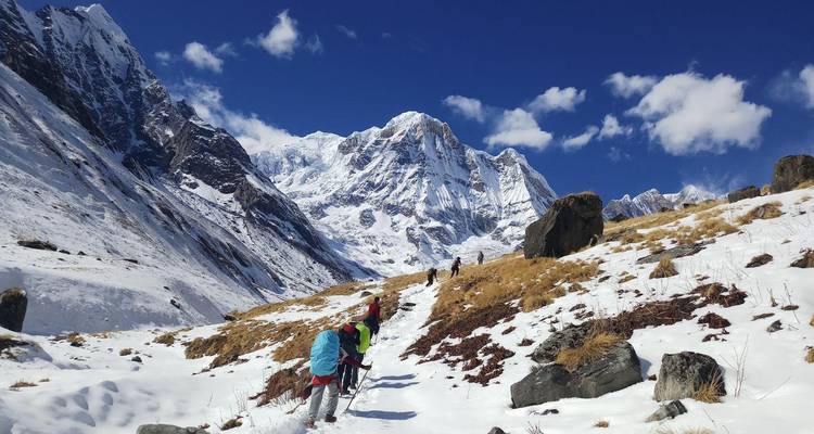 Trekkingstokers maken hun weg over een sneeuwwitte vallei met dramatische witte Himalayapicken die overal hoog uitsteken onder een hemel zonder wolken.
