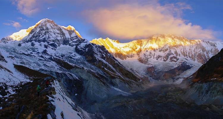 Gouden zonsopgang baadt de imposante Annapurna-pieken in warm licht terwijl trekkers over een sneeuwige berghelling hoog boven een gletsjer navigeren.