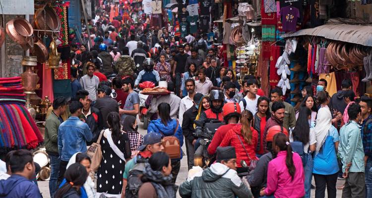 Druk bezochte marktstraat in Kathmandu vol met winkelende mensen, verkopers en levendige textiel.