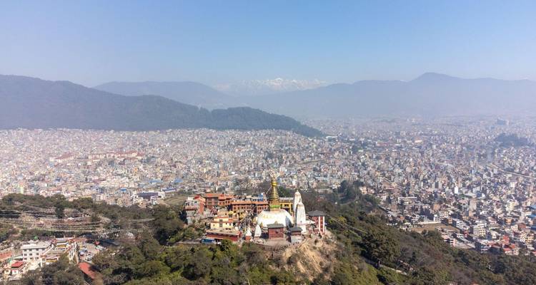 Luchtfoto van het Kathmandudal met de Swayambhunath Stupa op een groene heuvel, omringd door de uitgestrekte stadswijk en sneeuwtoppen in de verte.