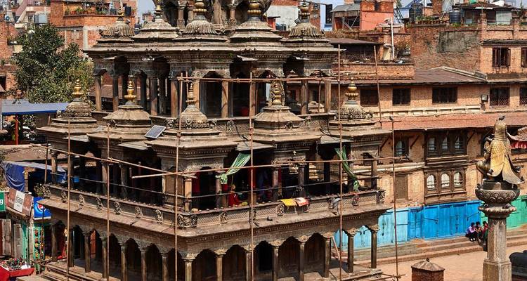 Historische stenen tempel in Patan die onder restauratie is met steigering op een zonnige dag.