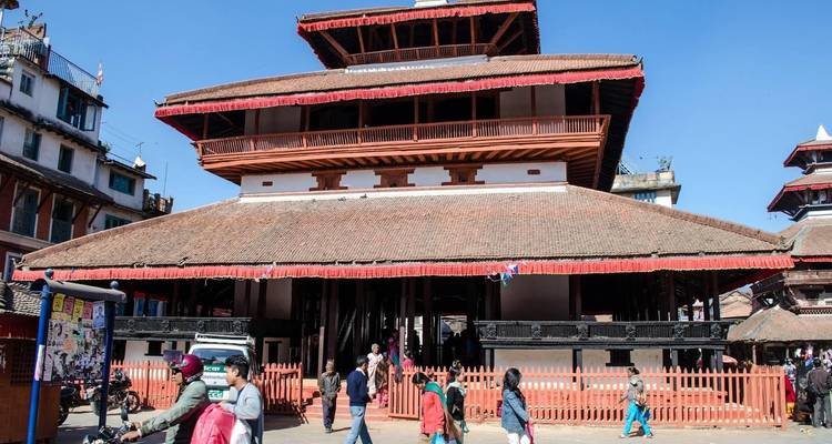 Mensen lopen voorbij een getrapt pagode-tempel op het Durbar Square in Kathmandu onder een heldere blauwe hemel.