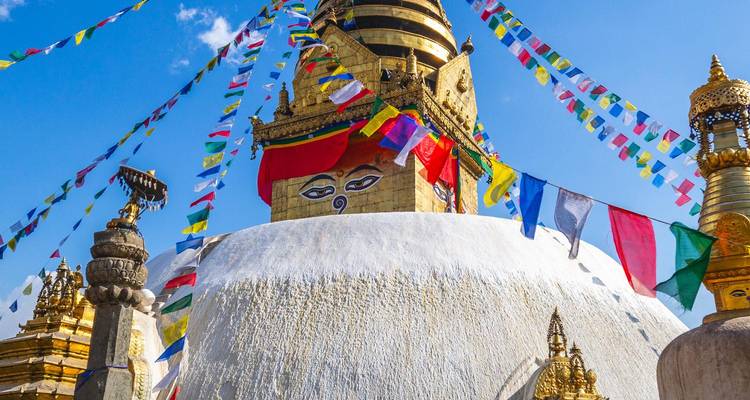 Close-up van de witte koepel en vergulde spits van Swayambhunath Stupa met kleurrijke gebedslinten tegen een diepblauwe hemel.