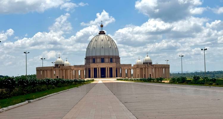 A long avenue leads to the grand dome of the Basilica of Our Lady of Peace under a bright sky.