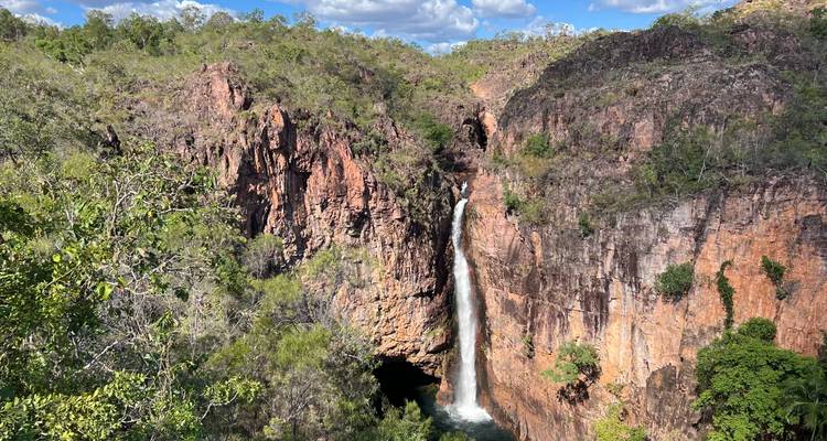 Una cascada alta y estrecha que se desploma sobre acantilados de roca roja escarpada hacia un desfiladero frondoso de bosque verde exuberante.
