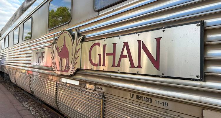 Auto plateado pulido del tren The Ghan con logo de camello y letras grandes a lo largo de la plataforma.
