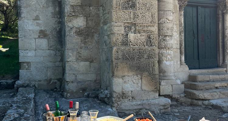 Rustikales Außenlunch-Setup mit Wein und lokalen Speisen auf einem Steintisch neben einem historischen Gebäude.