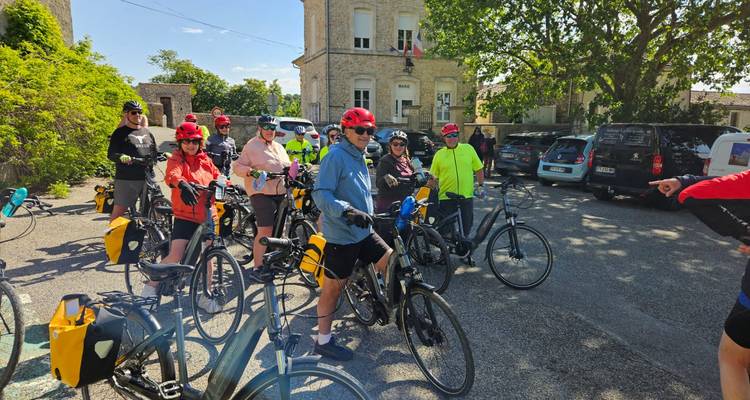 Eine große Gruppe von Radfahrern in farbenfroher Ausrüstung versammelt sich auf dem malerischen Dorfplatz, um eine Fahrt zu beginnen.