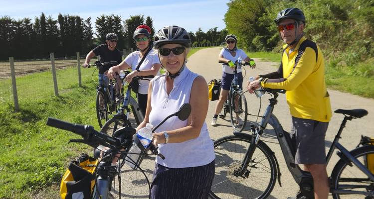 Eine kleine Gruppe von Radfahrern macht eine Pause auf einer ländlichen Straße, die von Feldern und Bäumen gesäumt wird, an einem sonnigen Tag.