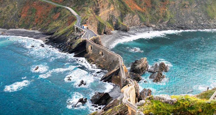 Vue en plongée de l'escalier en pierre et du pont en arc menant à San Juan de Gaztelugatxe entouré par une mer turquoise
