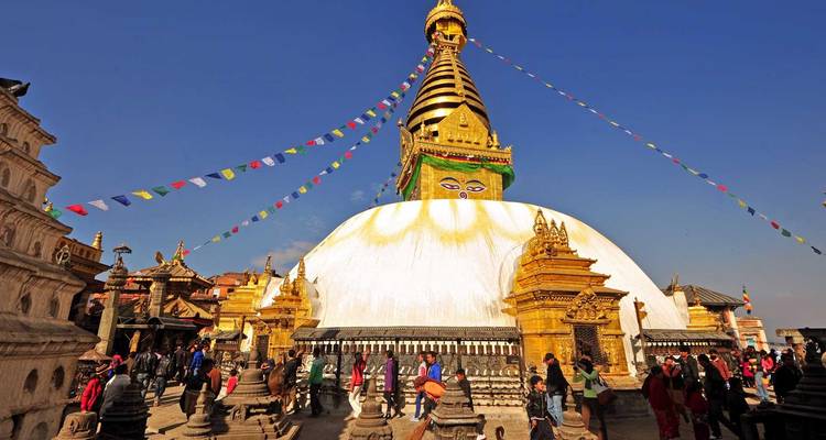 Stupa de Swayambhunath avec ses yeux de Bouddha emblématiques, ses drapeaux de prière et ses foules de visiteurs sous un ciel bleu