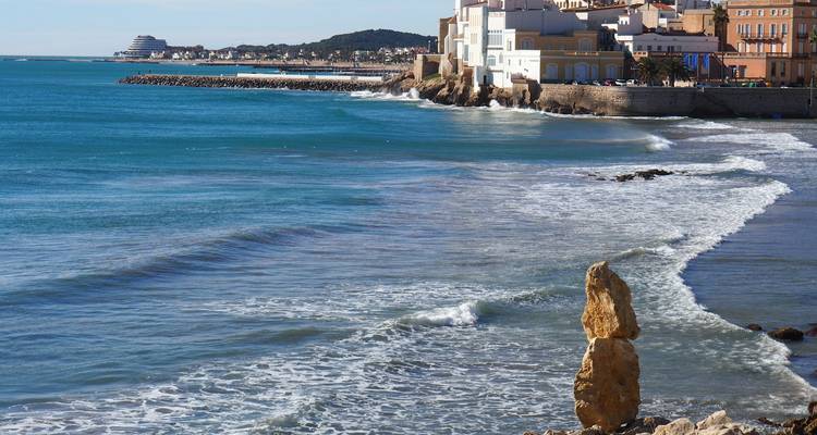 Turquoise Mediterranean waters lap against the coastal town of Sitges with cruise ship visible in the distance.