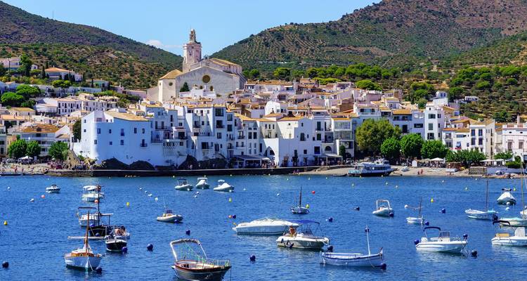 Picturesque whitewashed village of Cadaqués with boats anchored in the blue bay under clear skies.