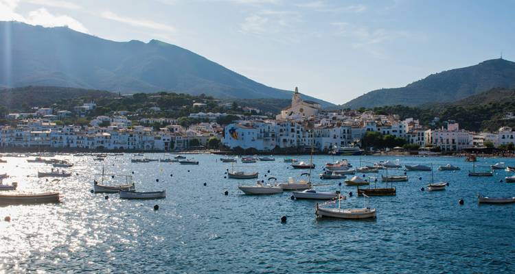Afternoon sun sparkles on the bay at Cadaqués with mountains silhouetted behind the town and scattered boats.