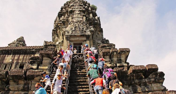 Menschenmengen von Touristen erklimmen eine steile Steintreppe zum in die Höhe ragenden Tempel von Angkor.