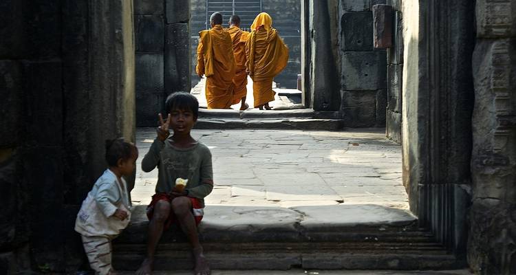 Kinder und wandernde Mönche, gerahmt durch antike Steintüren in einem Khmer-Tempel.