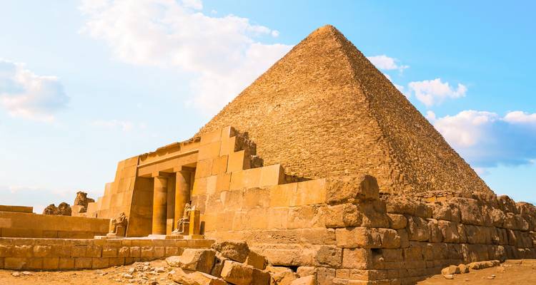 Gros plan aux teintes dorées d'une des grandes pyramides contre un ciel dégagé.