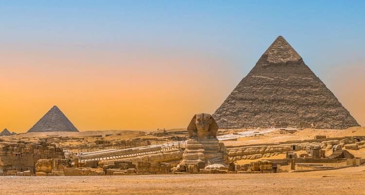 Vue classique du Sphinx avec les pyramides en silhouette au coucher de soleil doré.