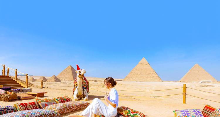 Le voyageur se détend sur des coussins colorés face aux pyramides sous un ciel bleu éclatant.