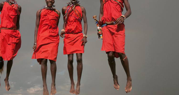 Maasai men mid-air while performing a traditional jumping dance against gray sky.