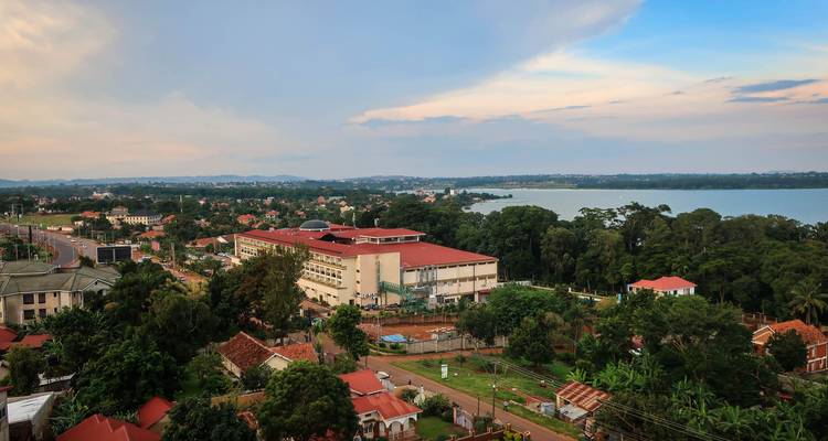 Elevated view of a lakeside Ugandan town with red roofs and greenery beside calm water.