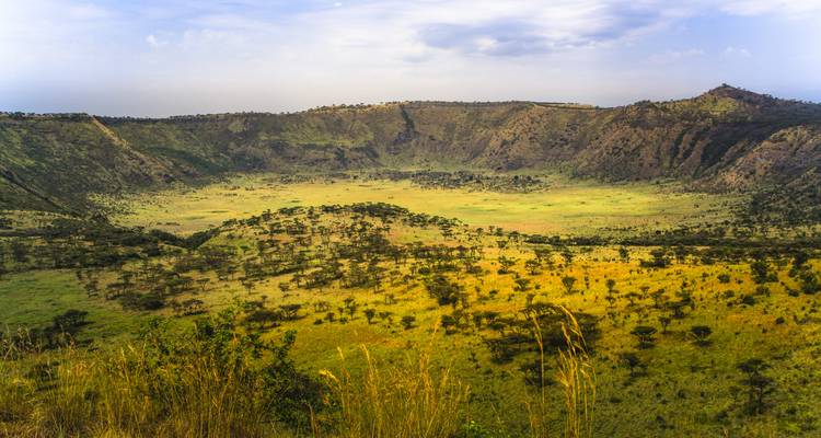 Expansive view into a grassy volcanic crater surrounded by rugged ridges and blue sky.
