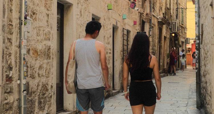 Paar spaziert durch eine enge Steingasse, die von historischen Kalksteingebäuden in der Küstenregion Kroatiens gesäumt wird