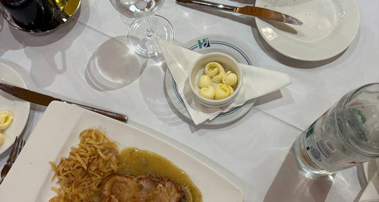 Draufsicht auf einen Restauranttisch mit angerichtetem Schweinefleisch, Sauce, Rösti und leeren Tellern