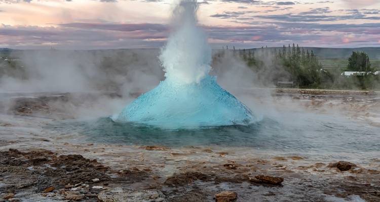 Türkisfarbene Kuppel des Strokkur-Geysirs, die sich Momente vor dem Ausbruch gegen einen Pastellhimmel wölbt