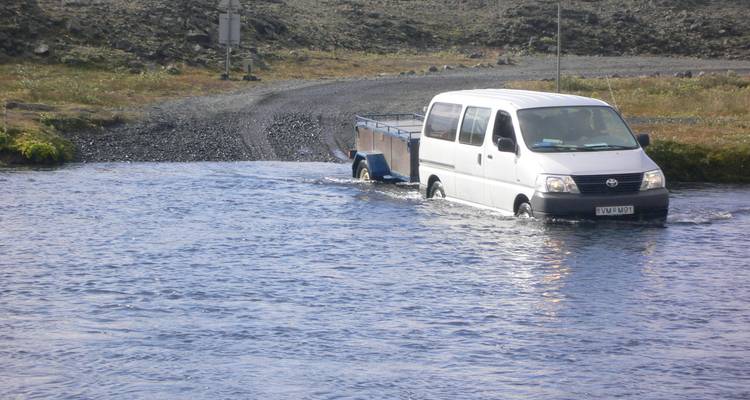 Furgoneta blanca con remolque atravesando un río poco profundo en un vado islandés