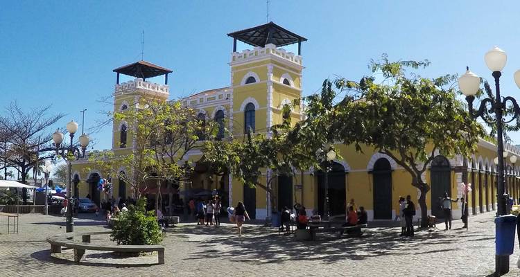 Histórico edificio del mercado público amarillo con torres gemelas y gente reunida en una plaza soleada