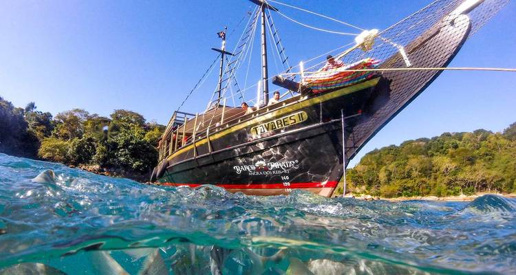Perspectiva a nivel del agua de un barco de tour negro navegando en un mar turquesa cristalino cerca de la orilla de la jungla