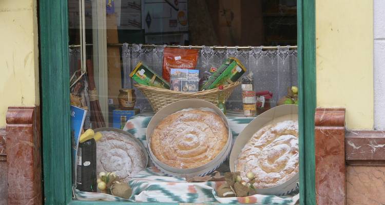 Das Schaufenster einer Bäckerei zeigt drei runde, mit Puderzucker bestäubte Ensaimadas und lokale Gourmetprodukte.