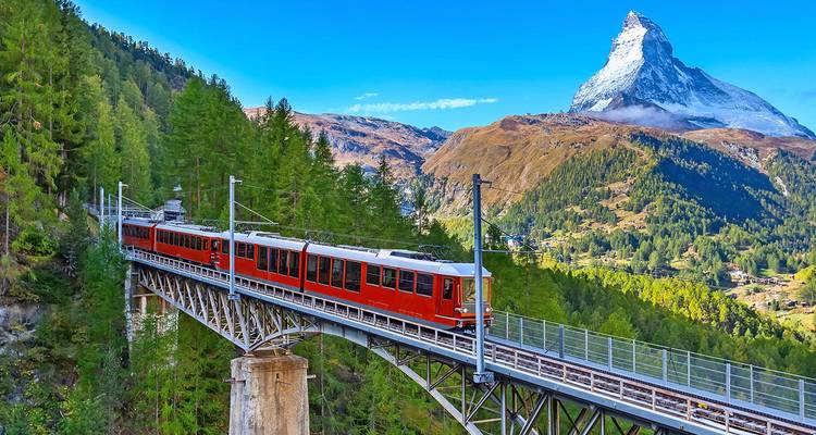 Red train crossing alpine bridge with majestic Matterhorn peak in background