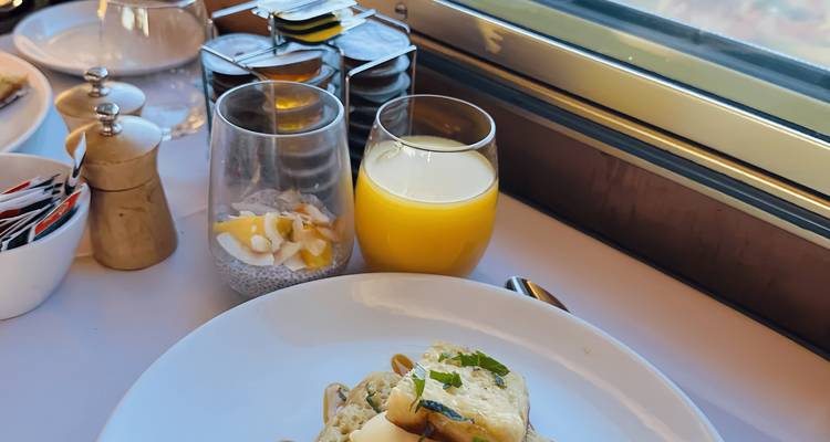 Plato de desayuno con jugo y pudín de chía junto a una ventana en el coche comedor de un tren