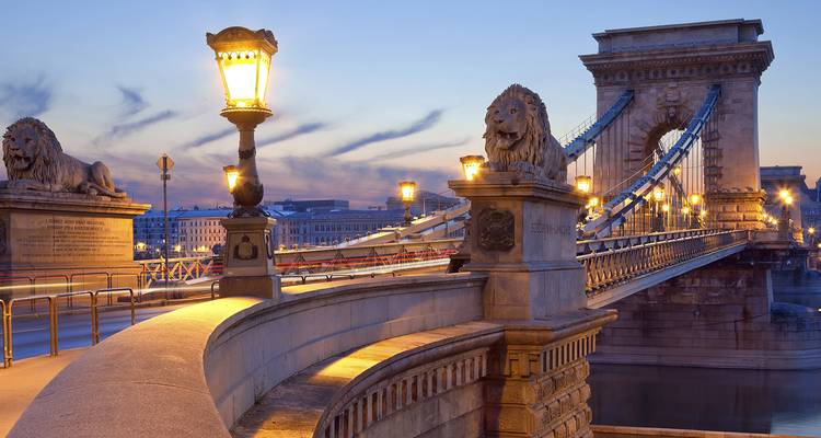 Evening view of the illuminated Chain Bridge with stone lion statues and the Danube River in Budapest.